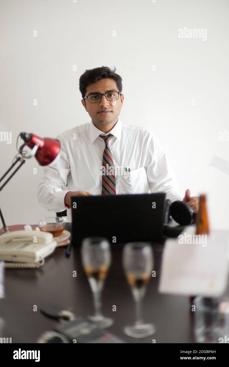 Indische Bengali groß, dunkel, hübsch Brünette junge Mann im Büro tragen genießen Erfolg, während auf einem Bürotisch in einem Büro / bpo sitzen Stockfoto