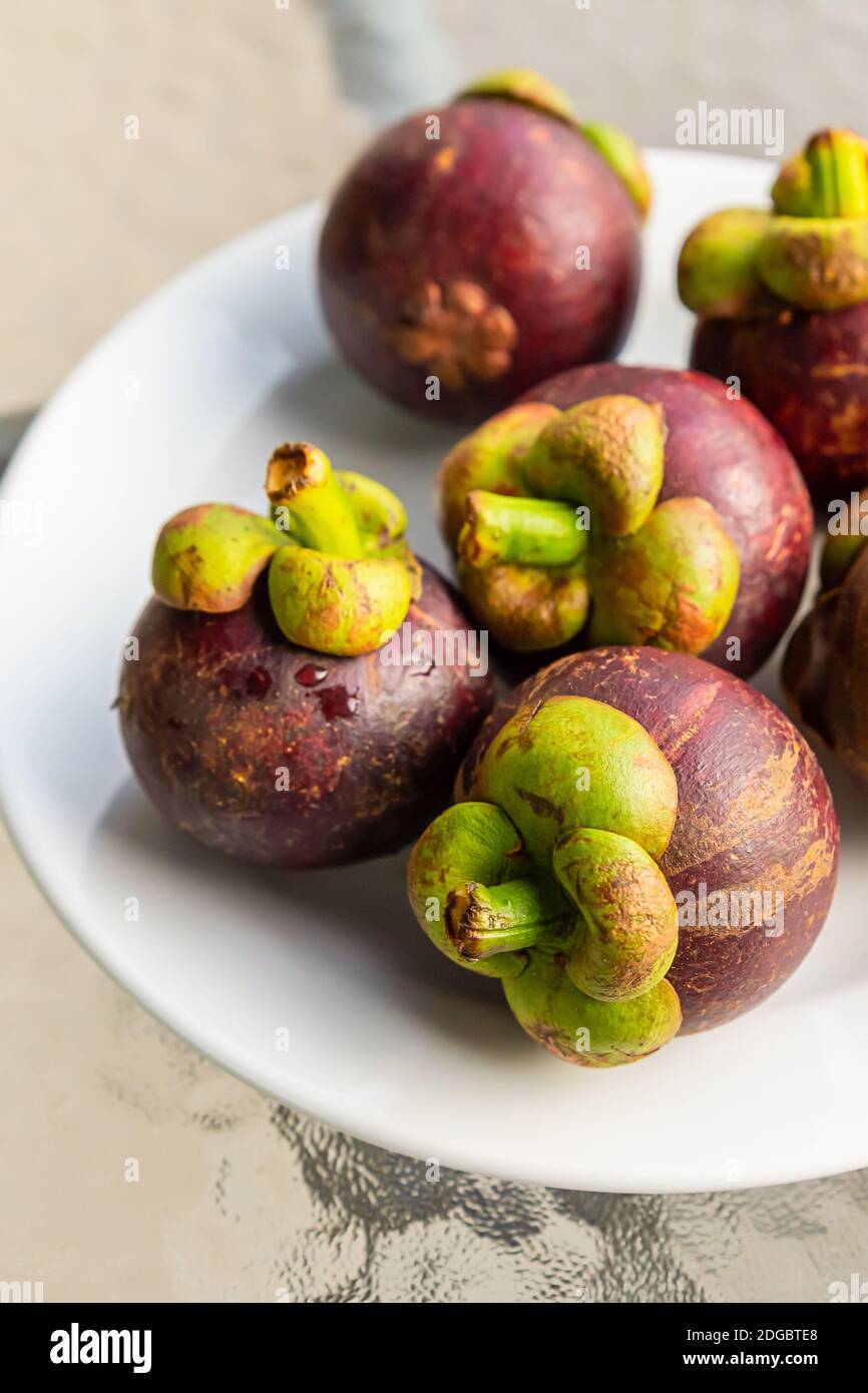 Frische Mangostan ganze Frucht liegt auf einem weißen Teller close-up Vertikales Foto Stockfoto
