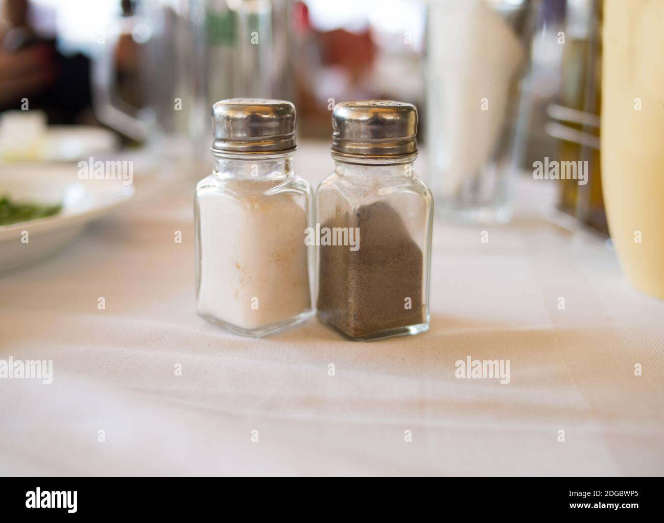 Salz und Pfeffer in einem transparenten Glasbehälter auf einem Tisch zur Mittagszeit auf einer weißen Tischdecke Spic Stockfoto
