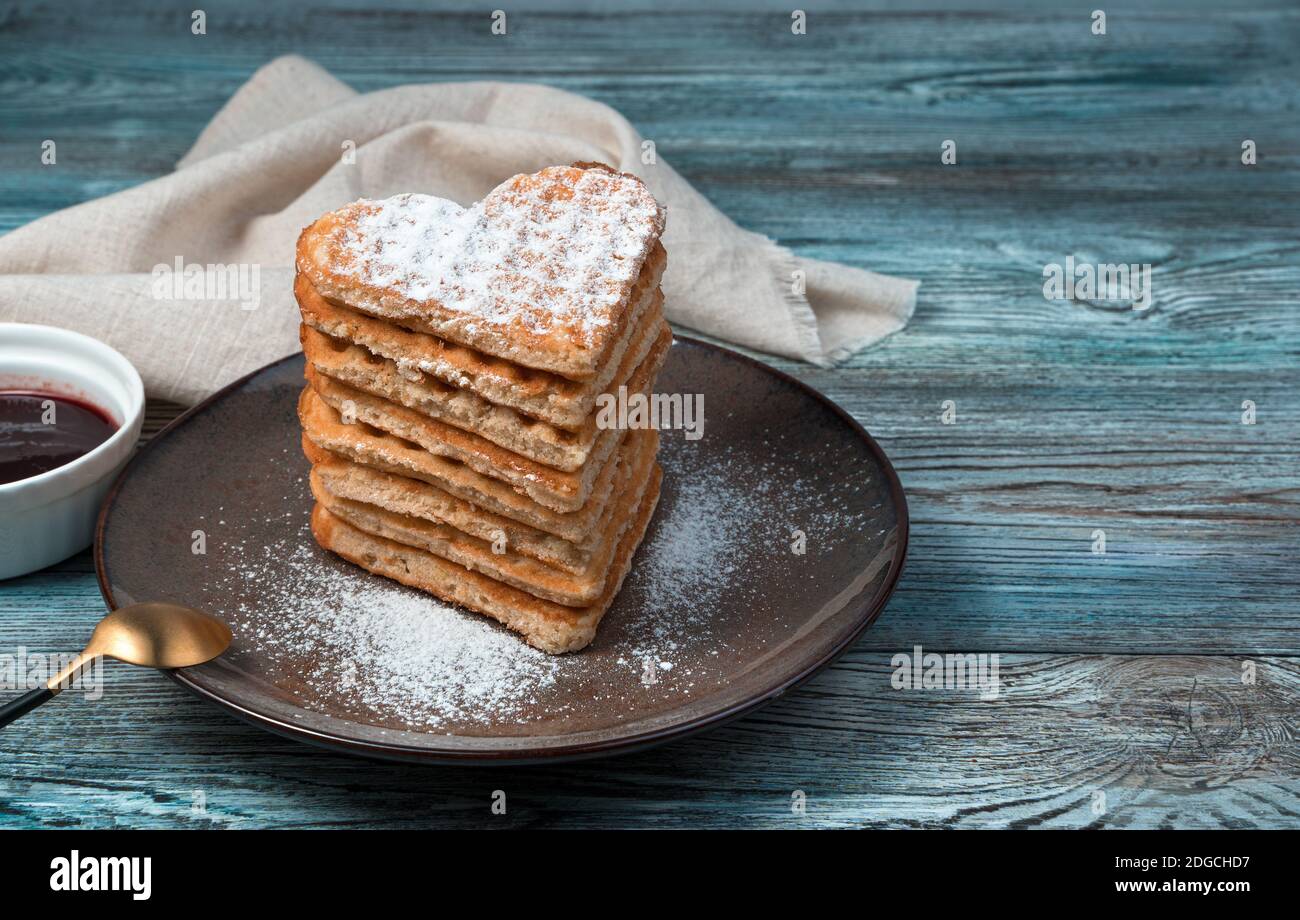 Ein Stapel herzförmiger Waffeln, bestreut mit Puderzucker auf einem hölzernen Hintergrund. Stockfoto
