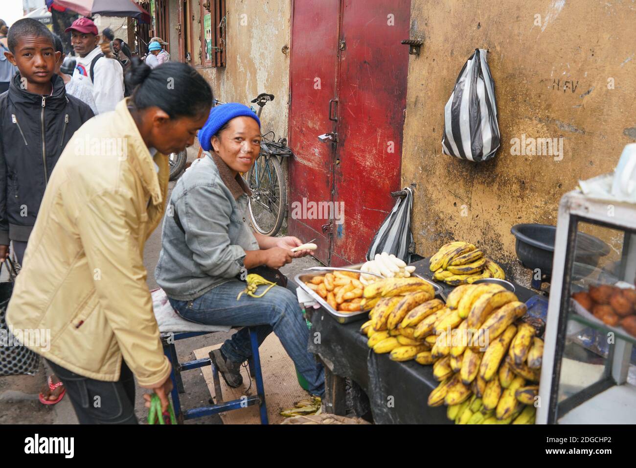 Antananarivo, Madagaskar - 24. April 2019: Unbekannte madagassische Frau, die auf der Straße Essen aus Bananen zubereitete, mehr Einheimische im Hintergrund. Typische sc Stockfoto