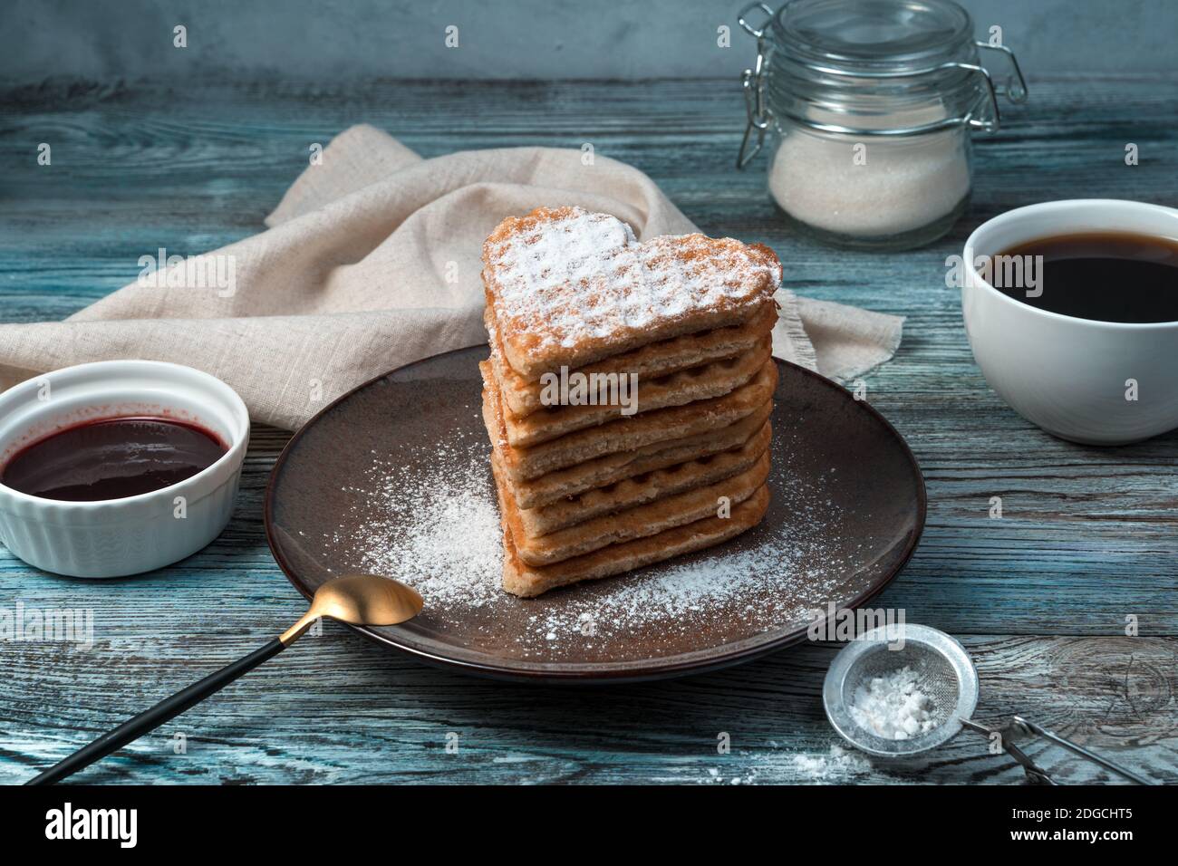 Wiener Waffeln in Herzform legten sie in einem Haufen auf die braune Platte auf grau-blauem Holzgrund. Stockfoto
