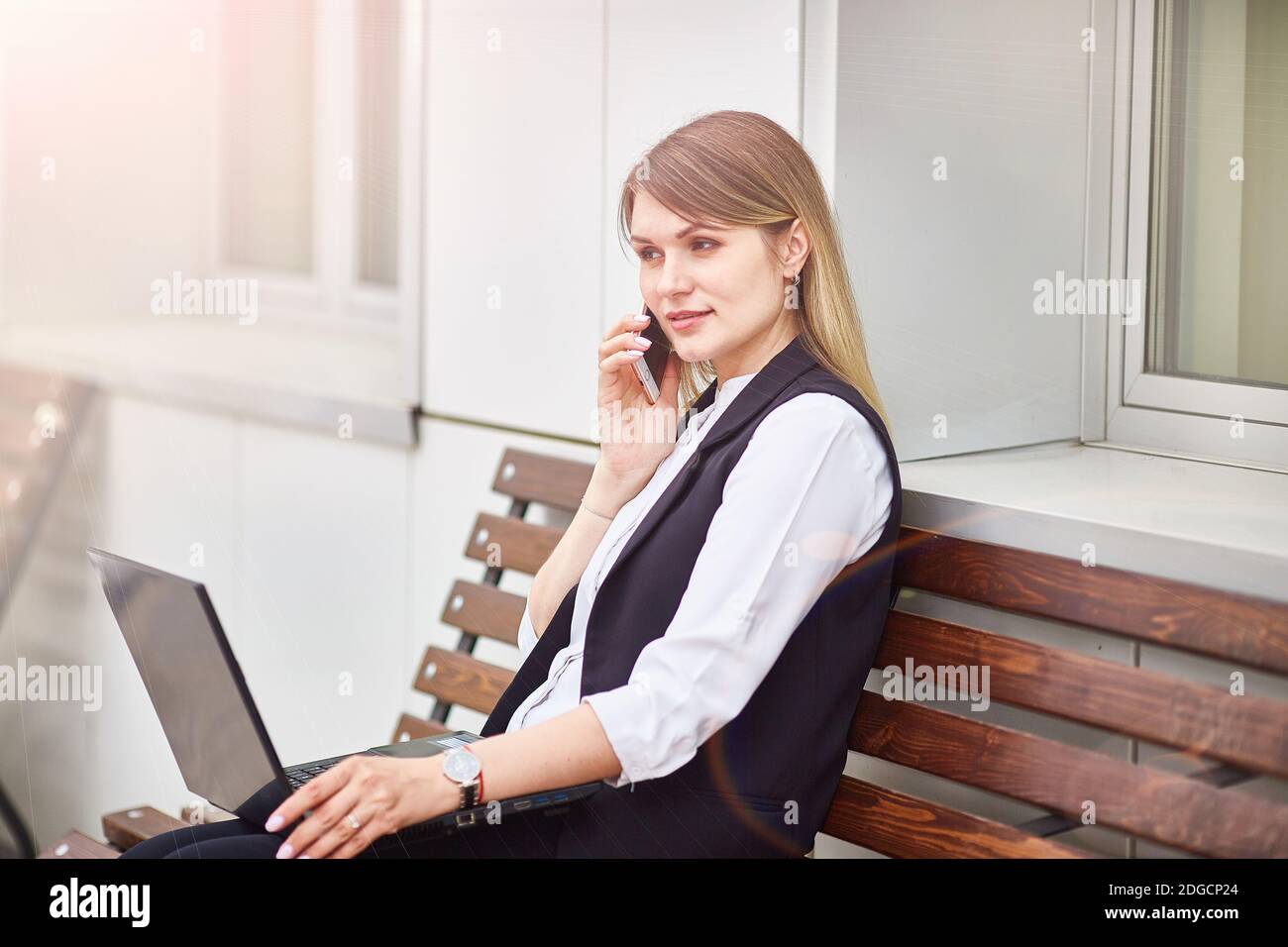 Mädchen sitzt auf einer Bank mit einem Laptop und sprechen Am Telefon Stockfoto