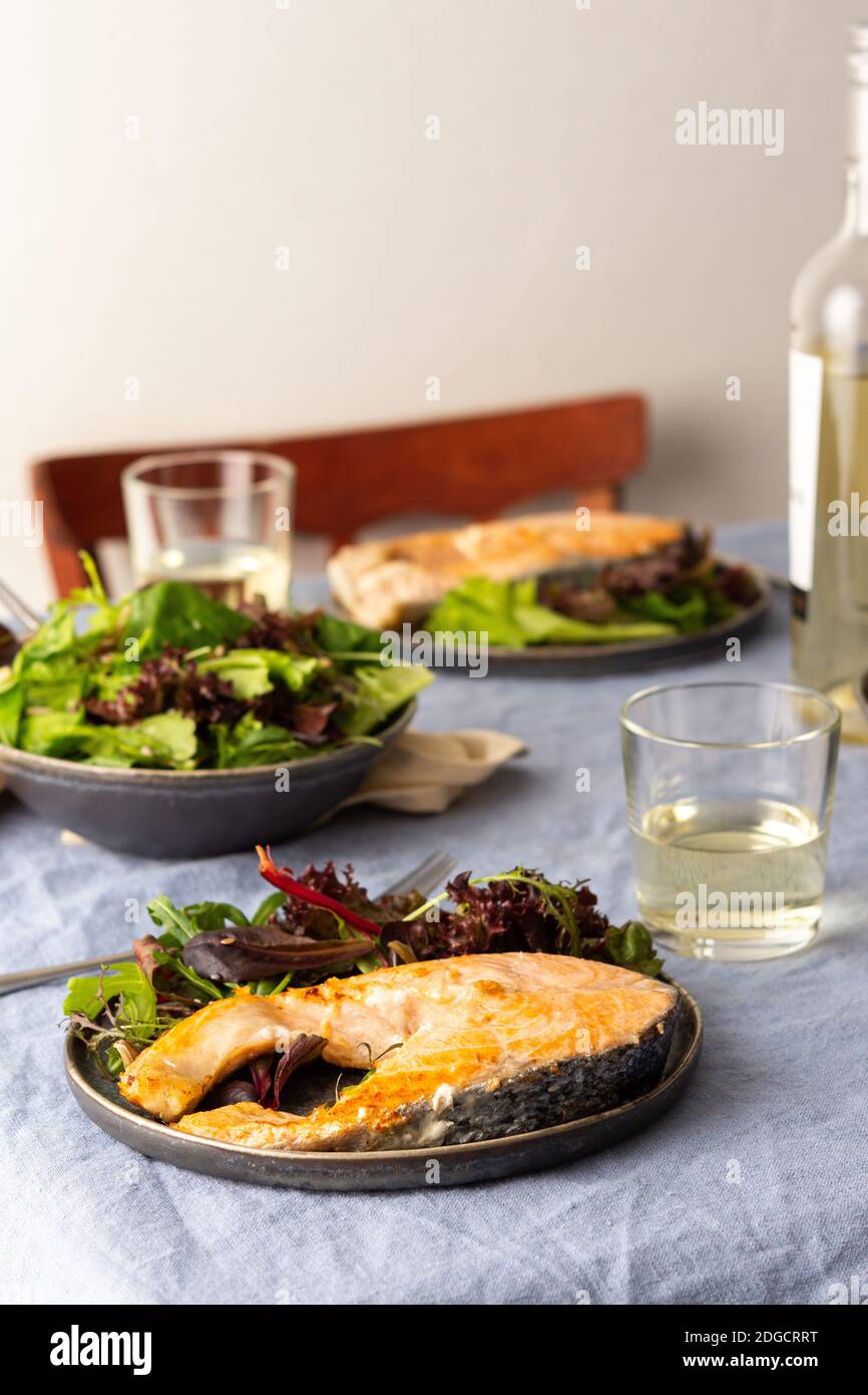 Gebratenes Lachssteak mit Salat auf einem Teller, Weißwein im Glas, leckeres herzhaftes Abendessen oder Mittagessen Stockfoto