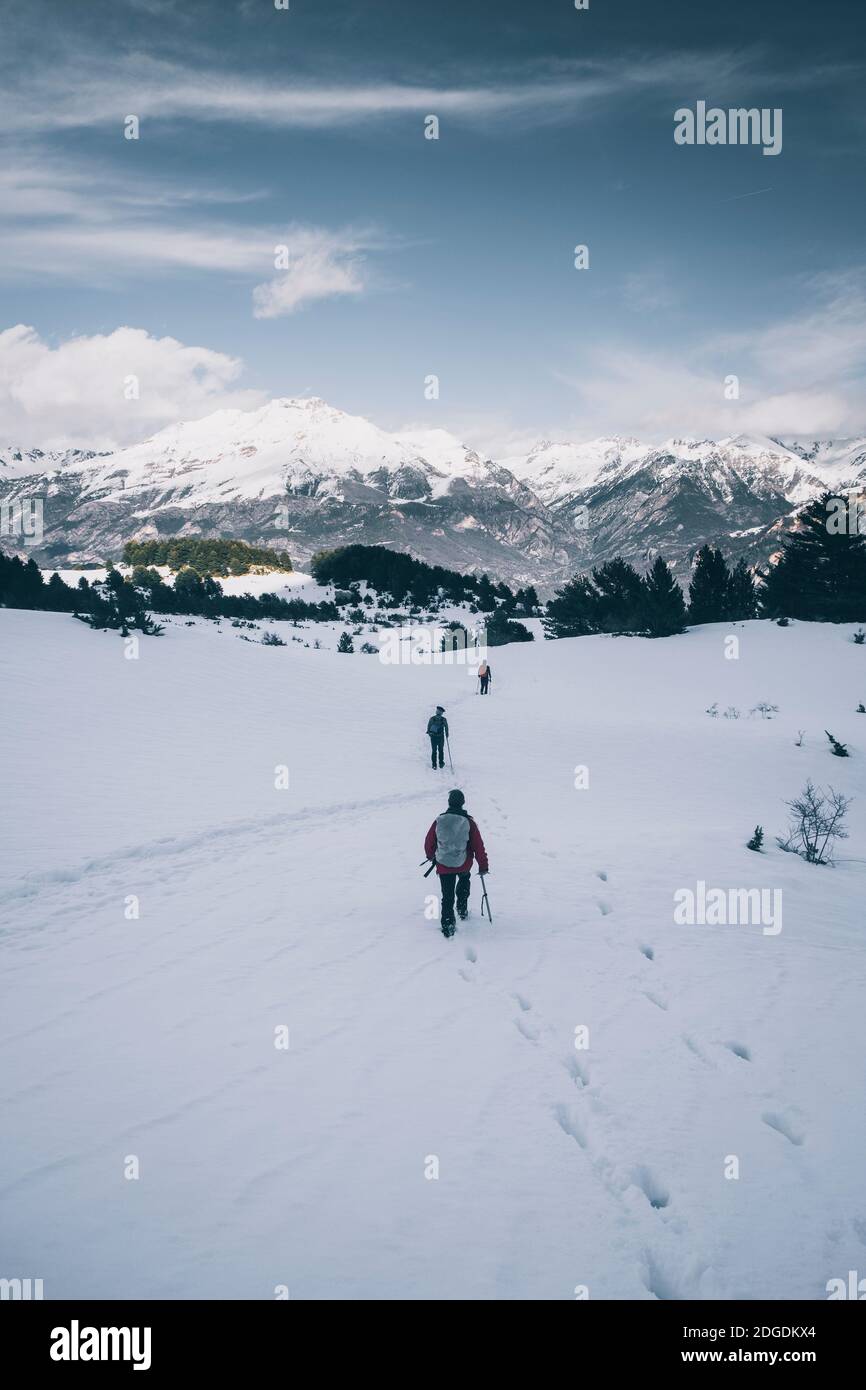 Eine Gruppe von männlichen Wanderern, die auf einem verschneiten Plateau gegen schneebedeckte Berge, Panticosa, Aragon, Spanien, wandern Stockfoto