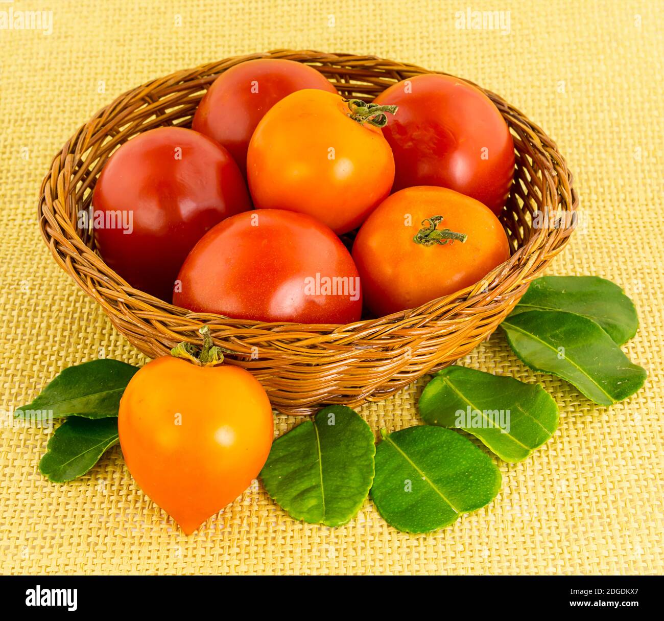 Große rote Tomate in einem Korbbraunkorb mit einem Herzförmige Frucht mit grünen Blättern aus der Nähe Stockfoto