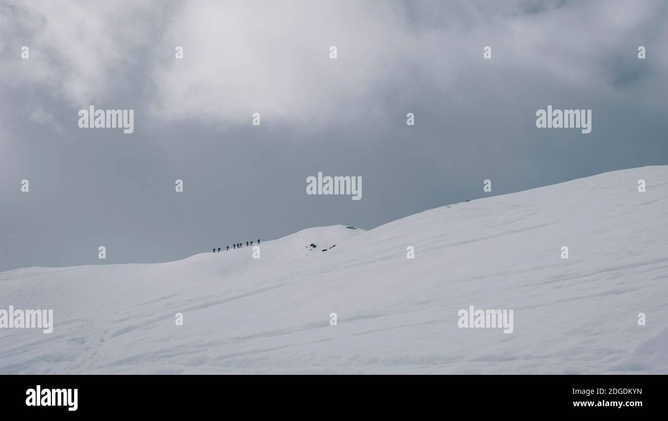 Eine Gruppe von Alpinisten versuchen, einen schneebedeckten Gipfel gegen den bewölkten Himmel in den französischen Pyrenäen zu besteigen. Stockfoto