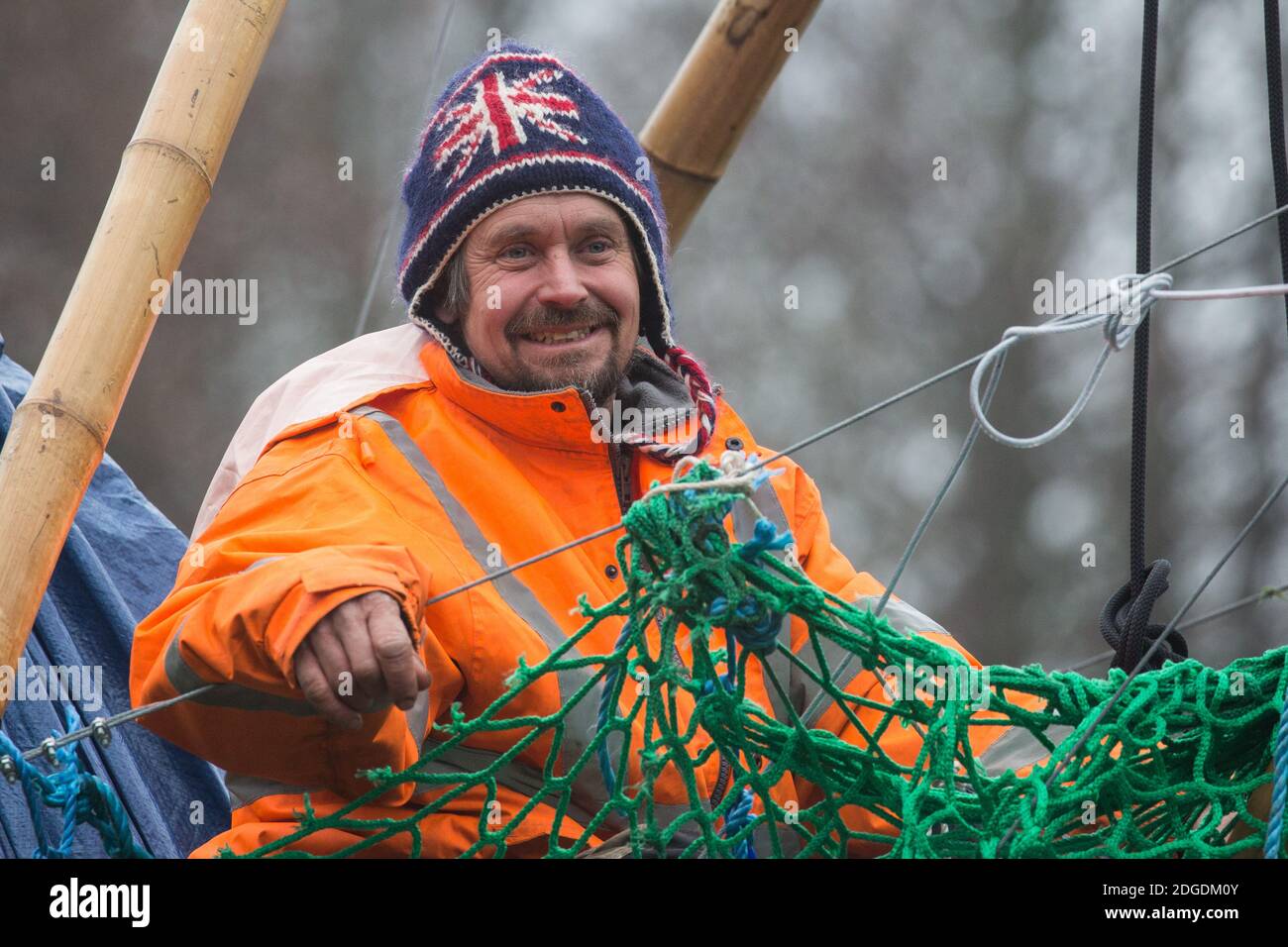 Denham, Großbritannien. Dezember 2020. Dan Hooper, in den 1990er Jahren weithin als Swampy bekannt, sitzt auf einem Bambusstativ im Fluss Colne. Der Klima- und Straßenaktivist hatte am Vortag das Stativ besetzt, um den Bau einer Brücke im Rahmen der Arbeiten für die umstrittene Hochgeschwindigkeits-Eisenbahnverbindung HS2 und eine große Sicherheitsoperation mit Beamten von mindestens drei Polizeikräften zu verzögern, Das Nationale Räumungsteam und die Sicherheitskräfte des HS2 wurden eingesetzt, um seine Entfernung zu erleichtern. Kredit: Mark Kerrison/Alamy Live Nachrichten Stockfoto