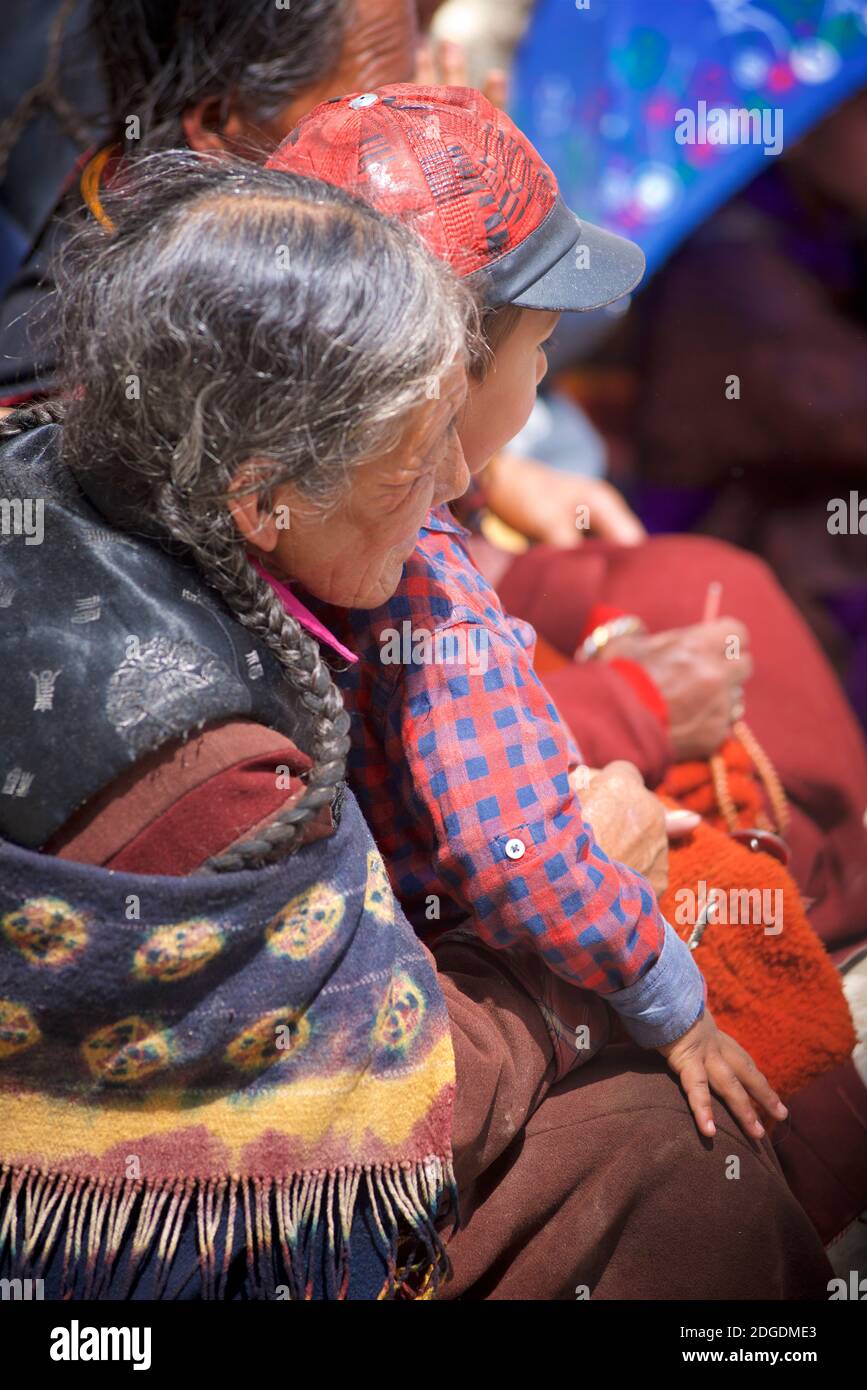 Ladakhi Großmutter mit Enkel auf dem Schoß. Auf dem Karsha Gustor Festival trägt sie traditionelle lokale Kleidung, einschließlich einer Krawatte gefärbten Wolltuch. Karsha Kloster, in der Nähe von Padum Zanskar Valley, Ladakh, Jammu und Kaschmir, Nordindien Stockfoto