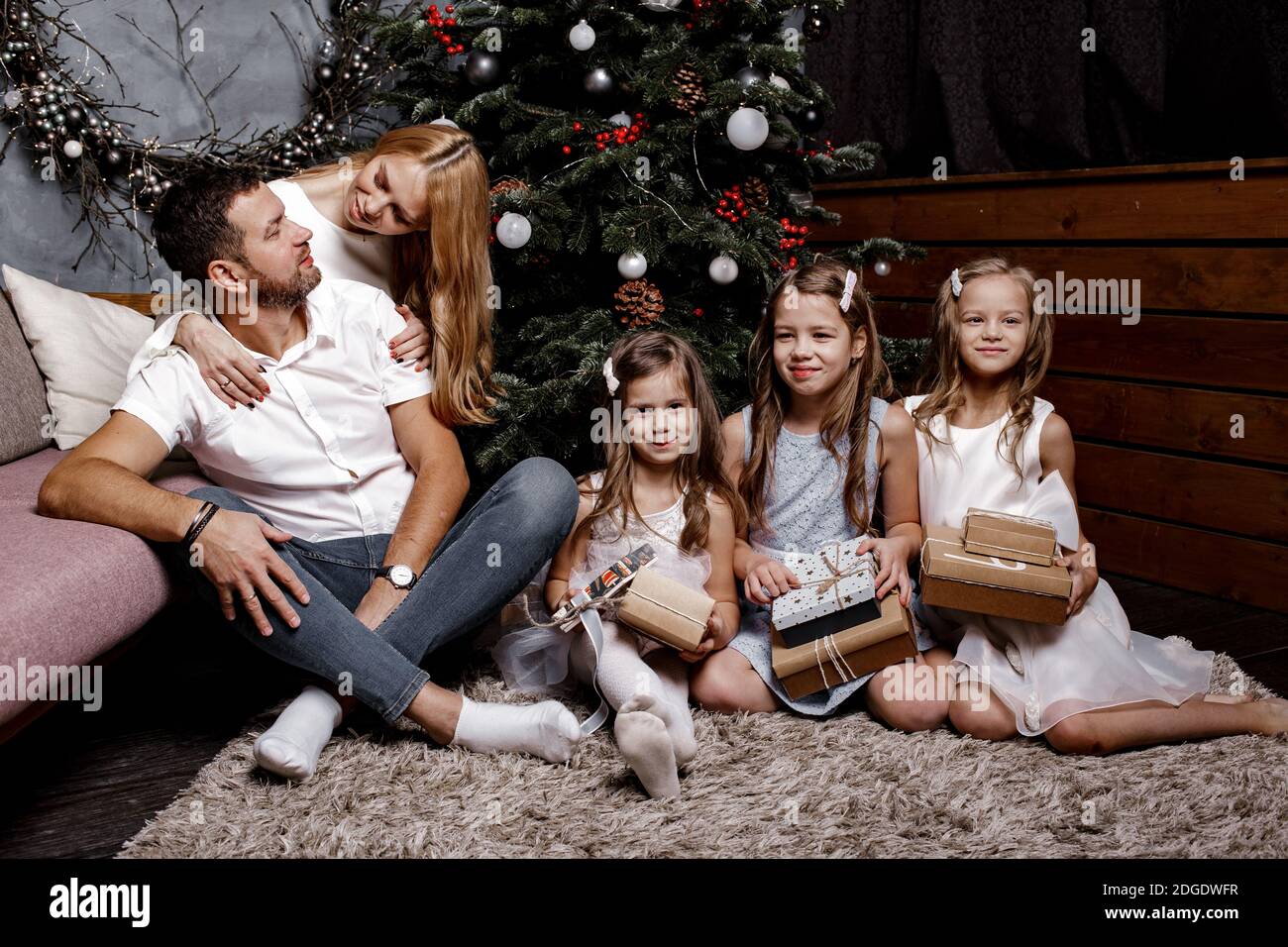 Glückliche nette Familie mit drei Kindern Austausch von Geschenken unter dem Weihnachtsbaum auf dem Teppich. Familien- und Urlaubskonzept. Stockfoto