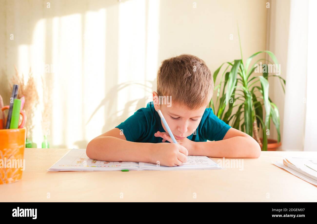 7 Jahre alt Kind Junge schriftlich im Arbeitsbuch sitzt am Schreibtisch in seinem Zimmer. Stockfoto
