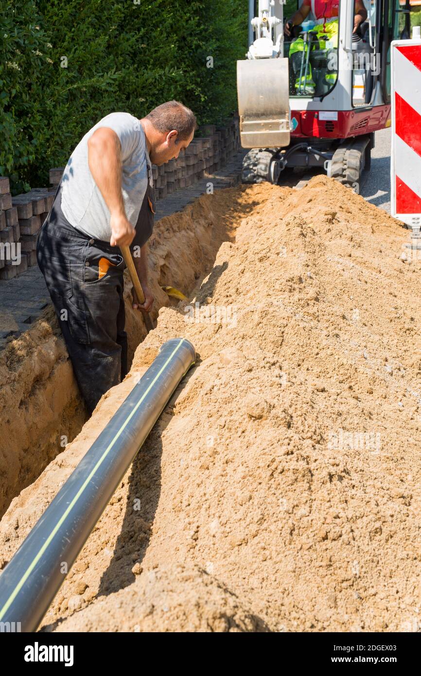 Arbeiter installieren unterirdische Glasfaserkabel in Straßenbaustelle Straßenaushub. Stockfoto