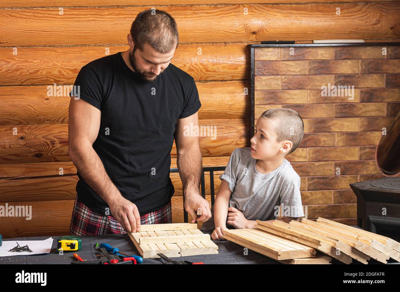 Vater und Sohn arbeiten an einem Holzprodukt und machen Markierungen für Befestigung, Werkzeuge und Holz auf dem Tisch in der Werkstatt. Tischlerei Trainingskonzept Stockfoto