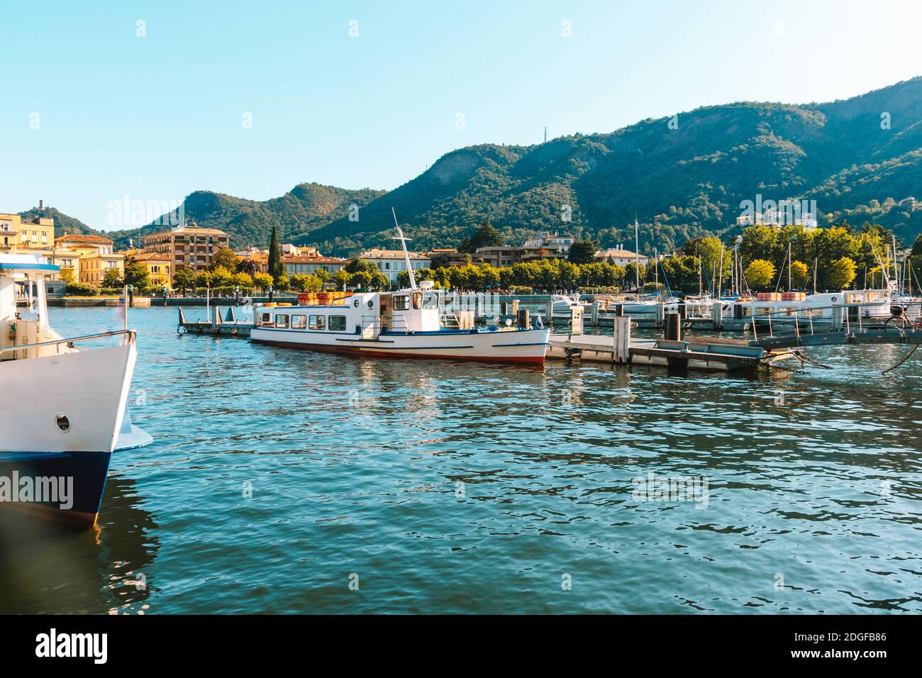Como See in der Stadt Como malerische Aussicht auf blaues Wasser mit weißen Yachten und Booten, Berge und schöne Stadtküste mit grünen Bäumen auf Summe Stockfoto