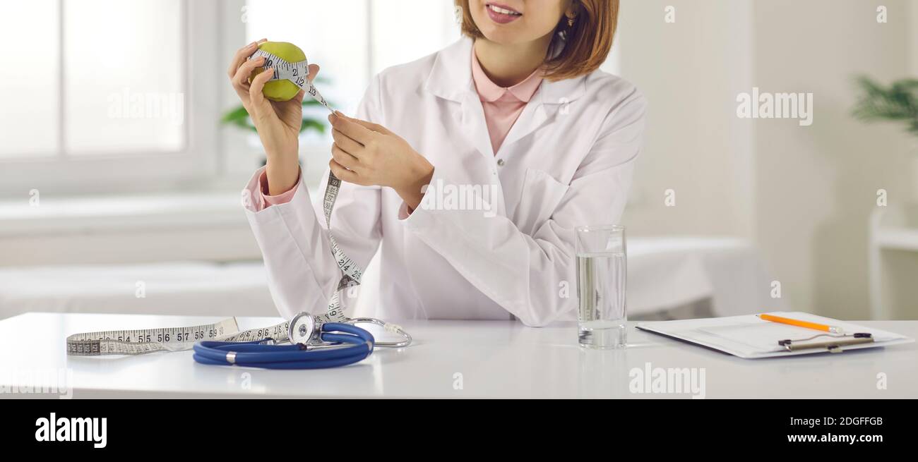 Junge Frau Arzt Ernährungswissenschaftler Messung Apfel mit Maßband wie Symbol für Schlankheitskur Stockfoto