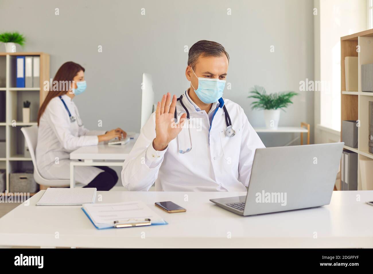Mann mittleren Alters Arzt in schützende medizinische Maske Kommunikation online Mit Patient Stockfoto