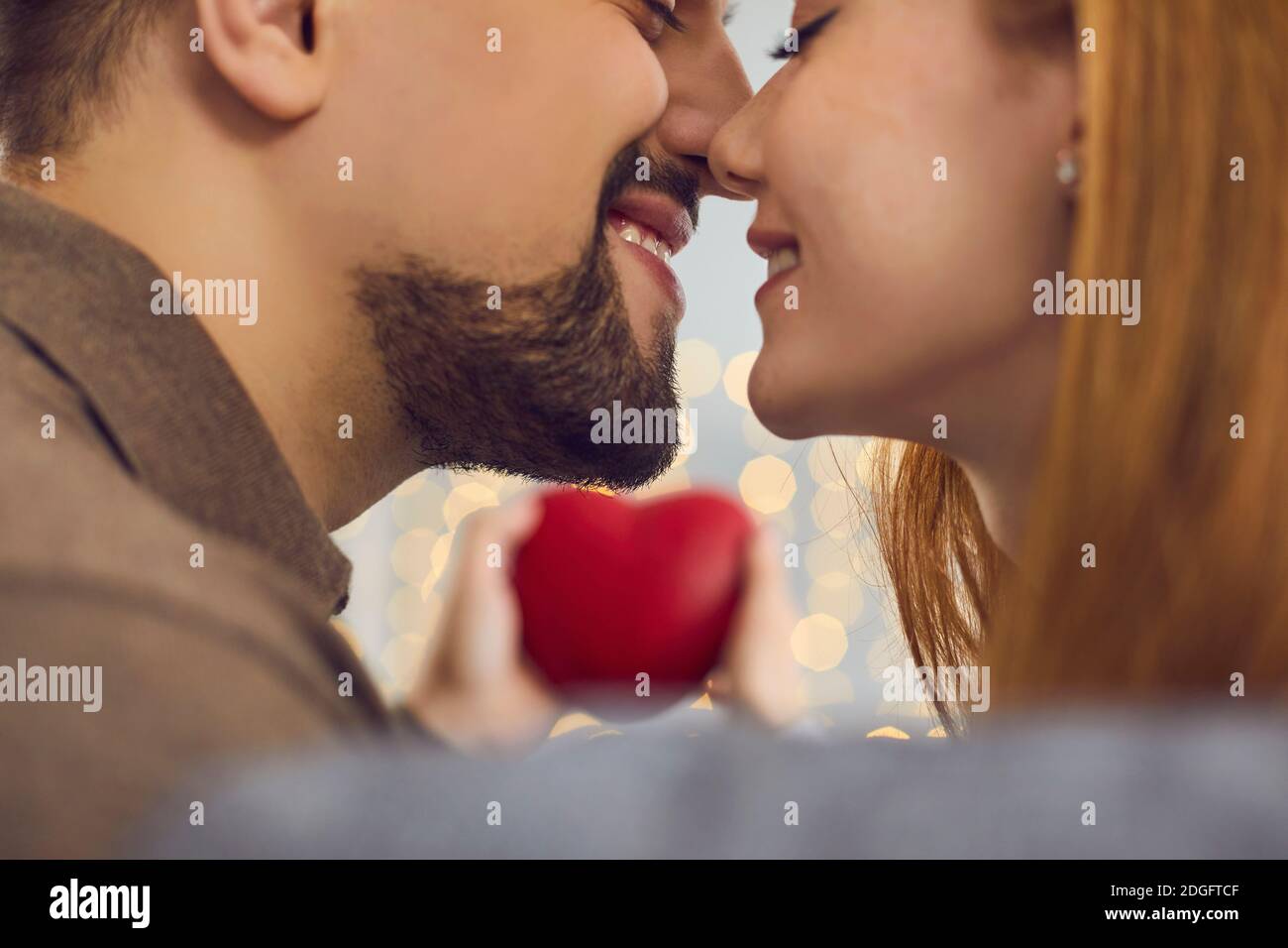 Glückliches junges Paar in der Liebe halten rotes Herz, lächeln und küssen am Valentinstag Stockfoto