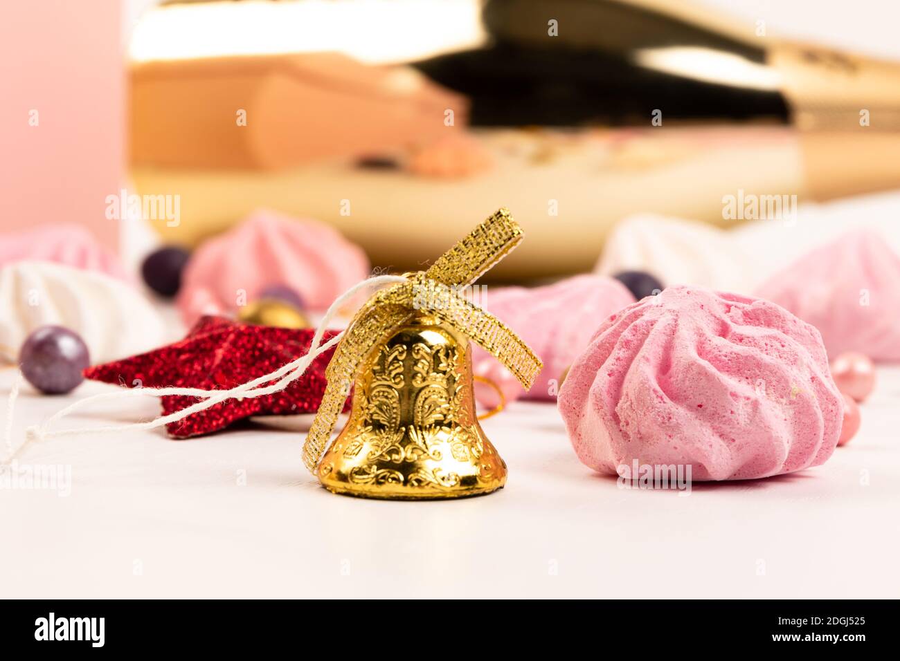 Bunte Dragee Bonbons, Glocke, Flasche Champagner, Kristallengel und Baiser Kuchen auf einem weißen Holztisch Stockfoto