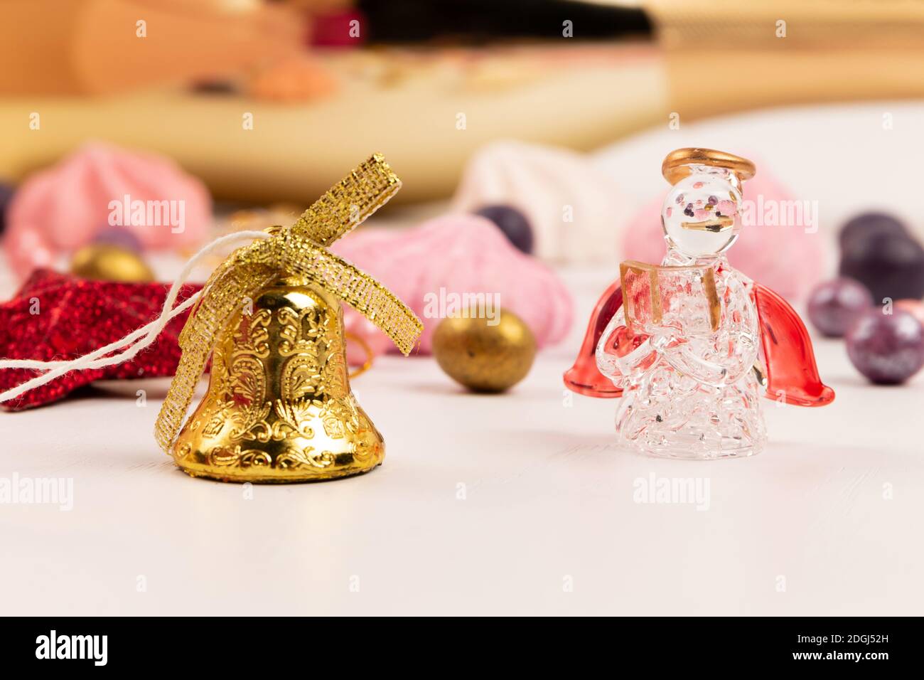 Bunte Dragee Bonbons, Glocke, Kristallengel und Baiser Kuchen auf einem weißen Holztisch Stockfoto