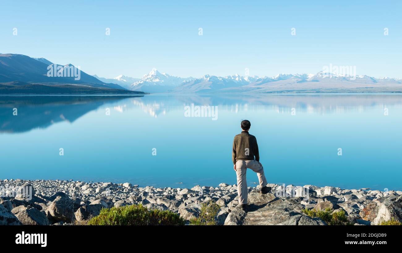 Tourist steht am Ufer des Sees Pukaki und beobachtet Mt Cook reflektiert in den klaren Gewässern Stockfoto