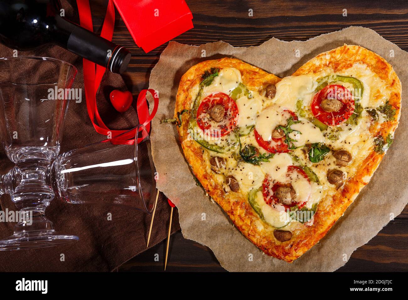 Pizza in Form eines Herzens und Wein mit Gläser auf dunklem Holzhintergrund Stockfoto