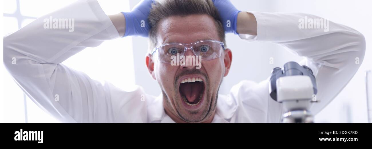 Mann in Schutzbrille und Gummihandschuhe zieht die Haare an Sein Kopf im chemischen Laborportrait Stockfoto