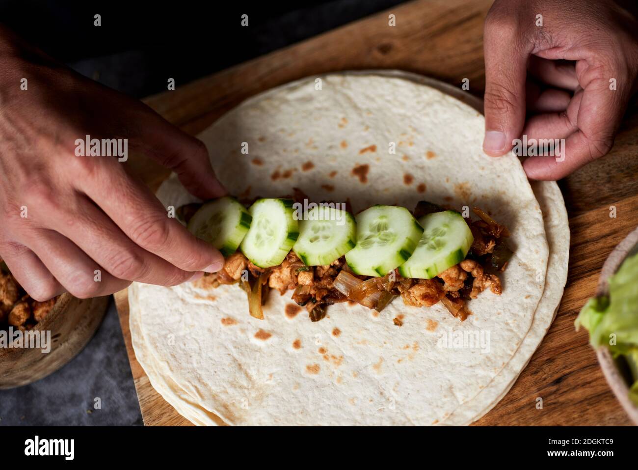 Blick in den hohen Winkel eines jungen Mannes, der ein Durum oder einen Burrito zubereitet, mit Hühnerfleisch, das mit verschiedenen Gemüsesorten wie Zwiebeln oder rotem und grünem peppe zubereitet wird Stockfoto