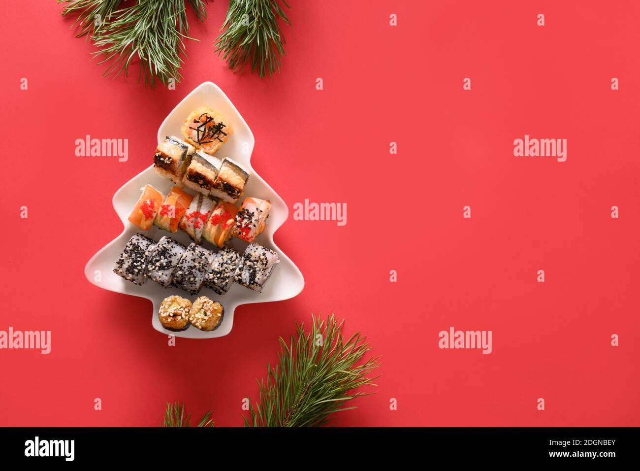 Sushi-Set in Teller als Weihnachtsbaum verzierten Tannenzweigen auf rotem Hintergrund. Blick von oben. Leerzeichen für Text. Flatlay-Style. Stockfoto