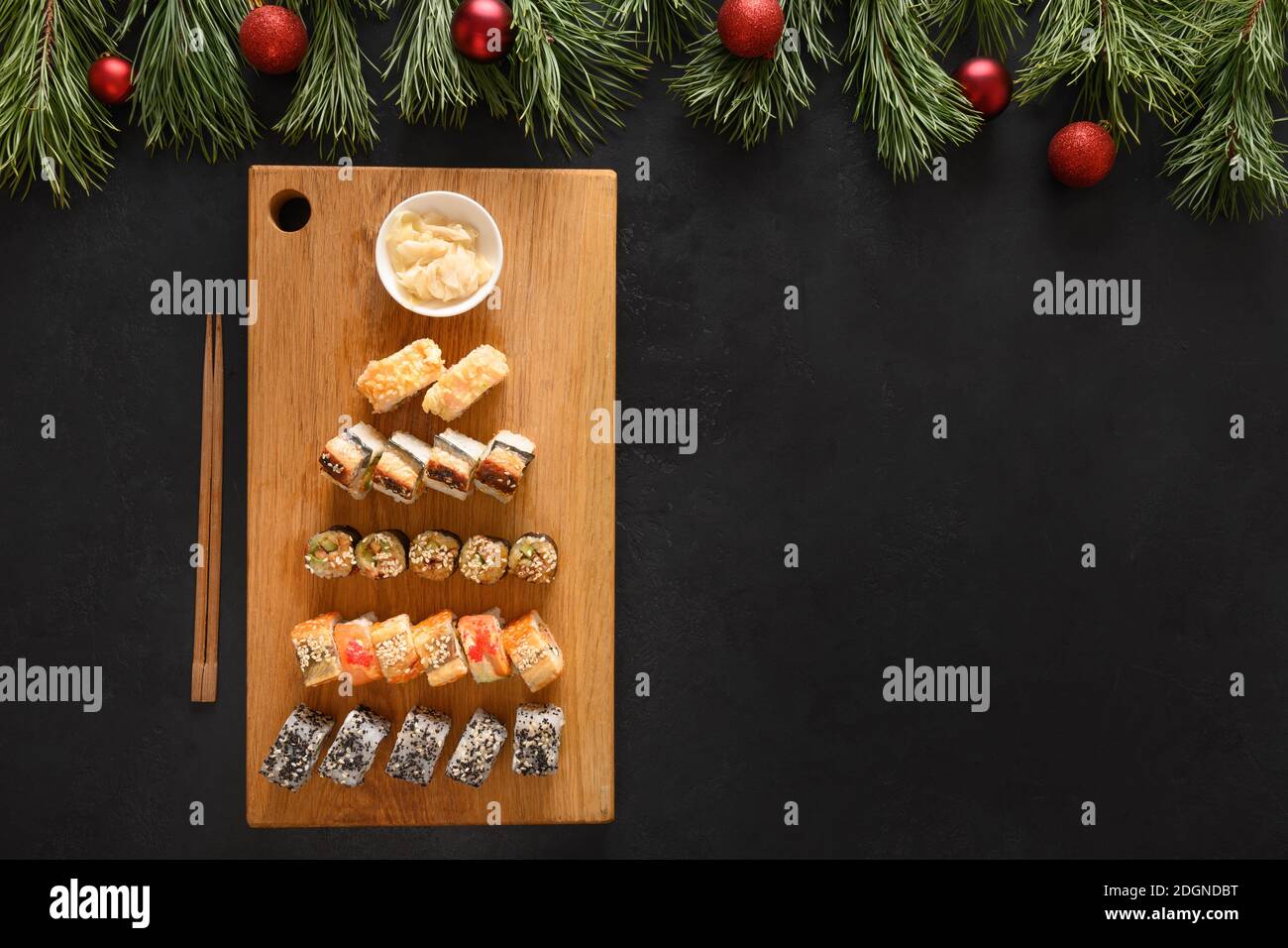 Sushi-Set als Weihnachtsbaum serviert auf Holz Schneidebrett als Weihnachtsdekoration auf schwarzem Hintergrund. Blick von oben. Leerzeichen für Text. Flache Lay-Optik. Stockfoto