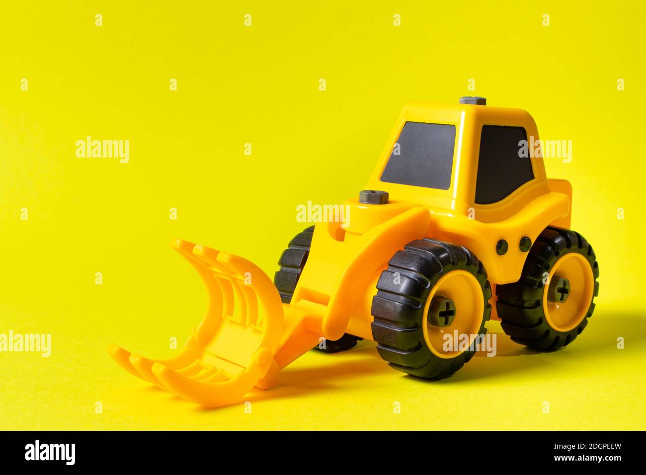 Kinderbaumaschine Holzlader auf gelbem Hintergrund. Traktor für den Jungen und Foto für den Spielwarenladen mit Platz für Textkopie Stockfoto