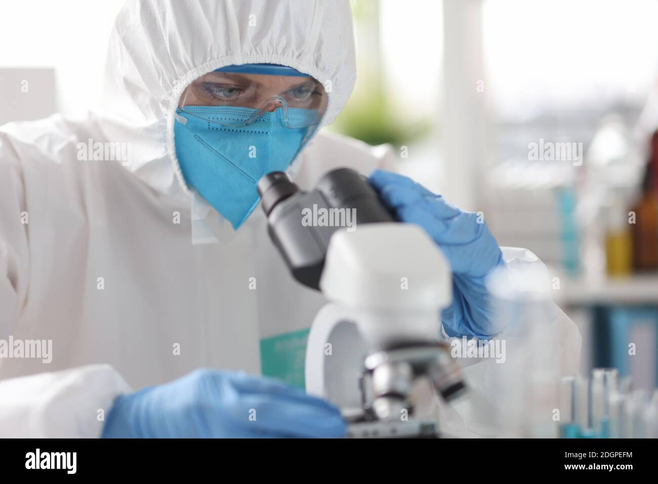 Wissenschaftler in Schutzanzug und Atemschutzmaske Blick durch Mikroskop in Labor Stockfoto