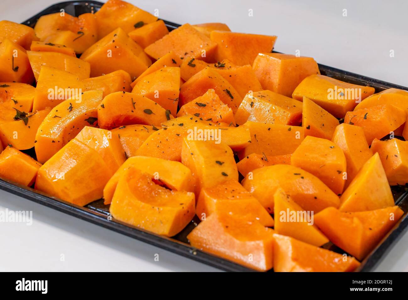 Nahaufnahme von Butternut-Kürbisstückchen, die zum Braten vorbereitet wurden, auf einem Backblech Stockfoto