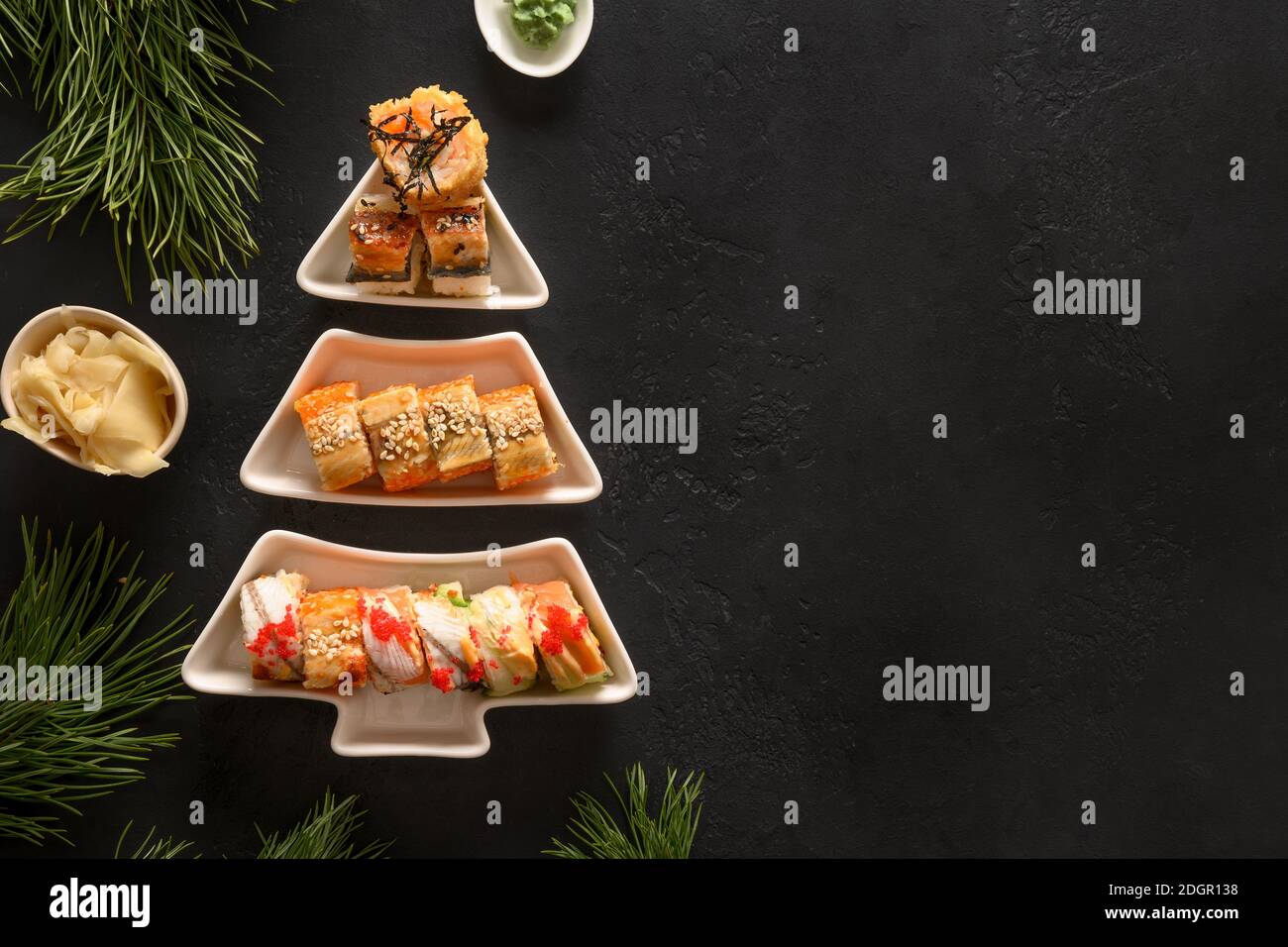 Sushi-Set serviert auf dem Teller als Weihnachtsbaum mit Weihnachtsdekoration auf schwarzem Hintergrund. Blick von oben. Leerzeichen für Text. Flache Lay-Optik. Stockfoto
