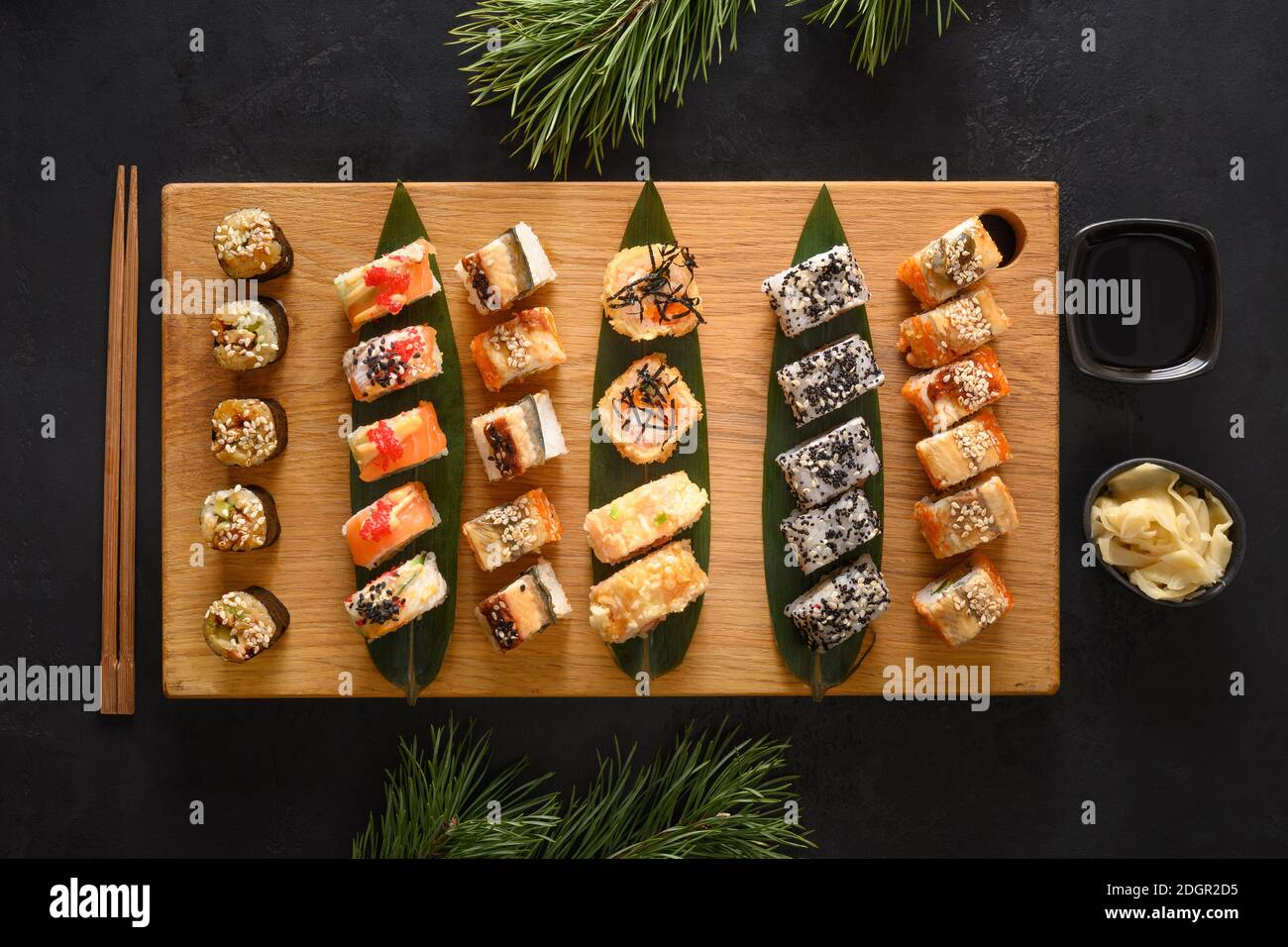 Weihnachtliches Sushi-Set auf Holzbrett mit Weihnachtsdekoration auf schwarzem Hintergrund. Blick von oben. Flache Lay-Optik. Stockfoto