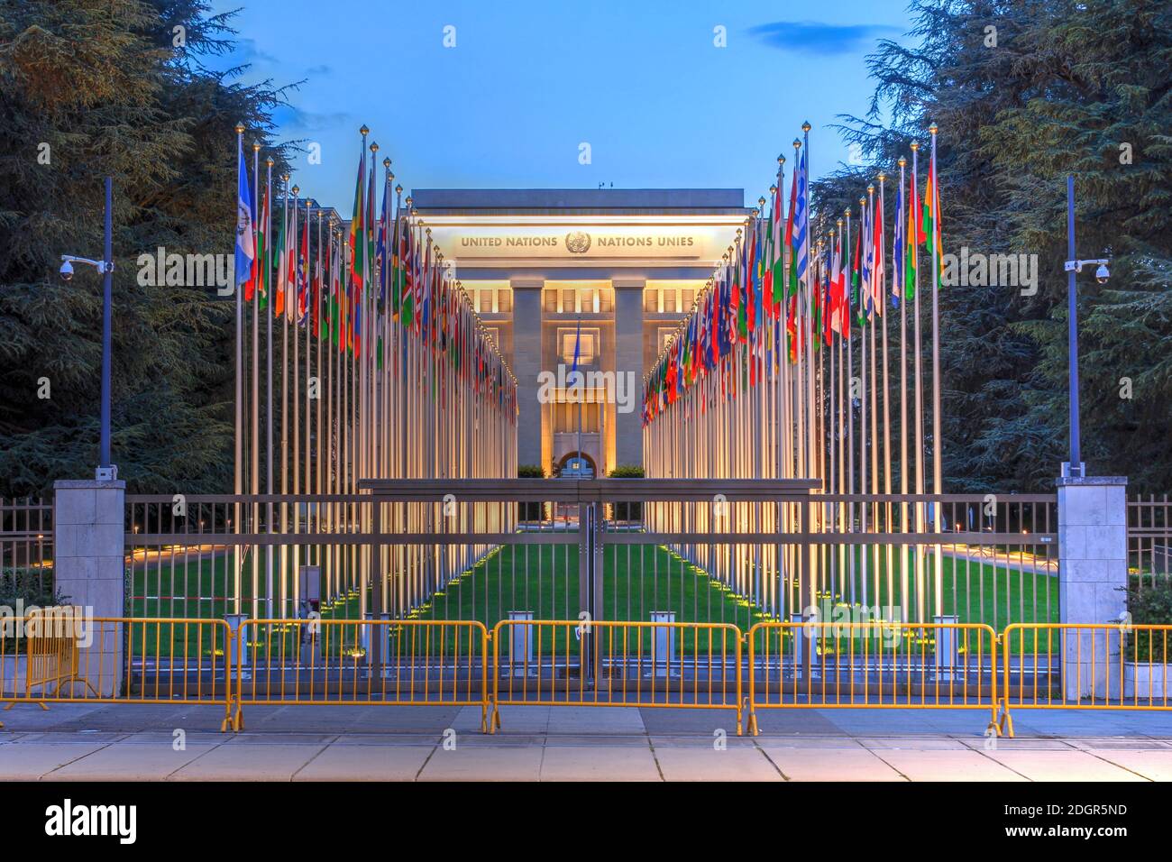 Büro der Vereinten Nationen von Genf (UNOG), Schweiz bei Nacht, mit dem Haupteingang A die Fahnenmasten der Mitgliedsstaaten. Stockfoto