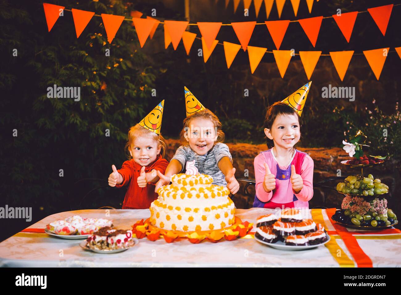 Kindergeburtstag. Drei fröhliche Kindermädchen am Tisch essen Kuchen mit den Händen und schmieren ihr Gesicht. Spaß Stockfoto