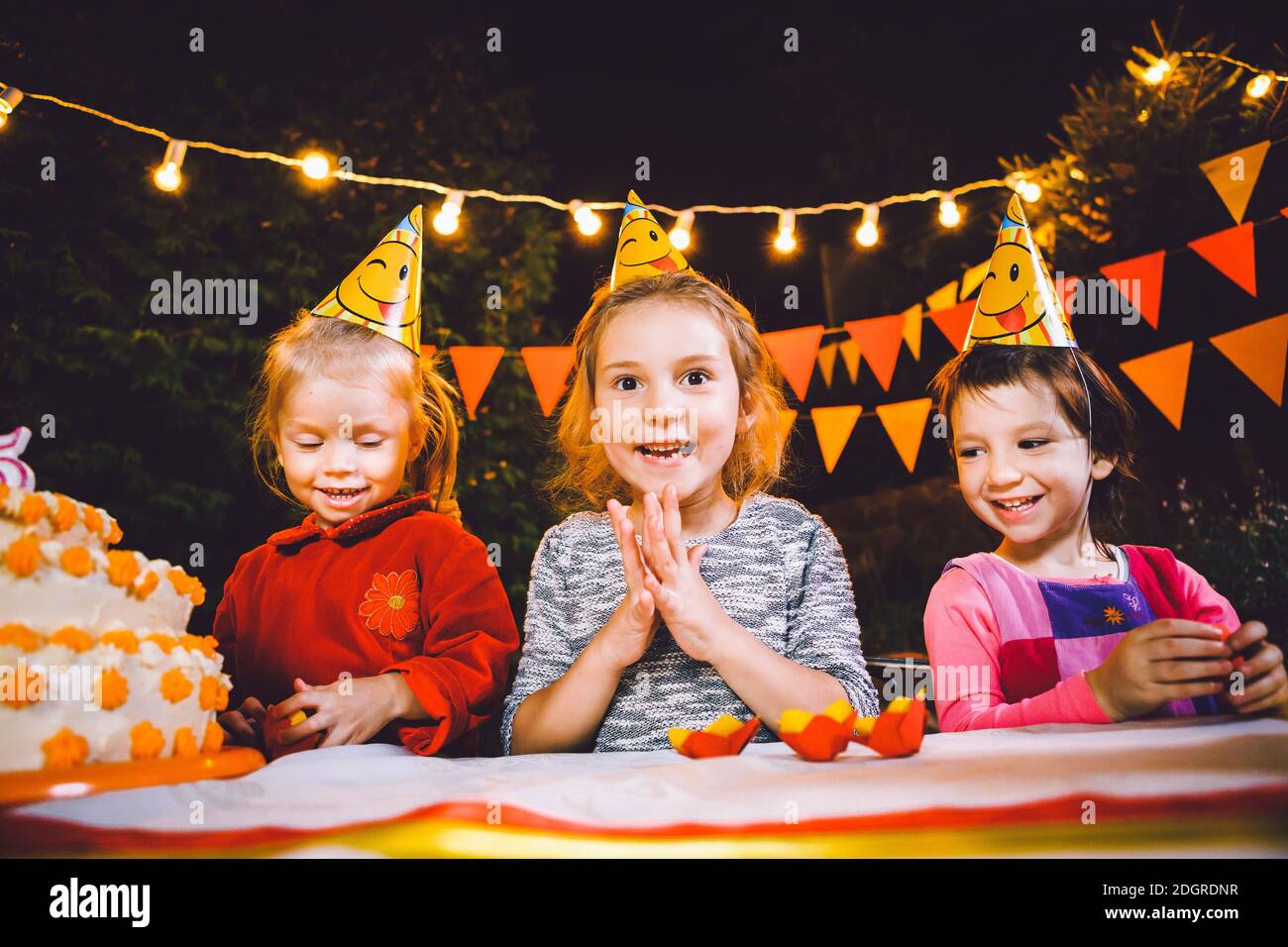 Kindergeburtstag. Drei fröhliche Kindermädchen am Tisch essen Kuchen mit den Händen und schmieren ihr Gesicht. Spaß Stockfoto