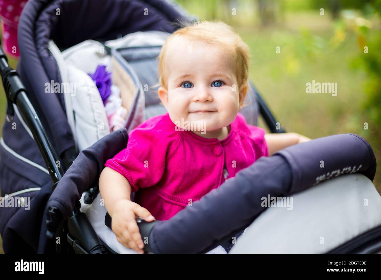Portrait eines kleinen lustigen Mädchen blonde mit blauen Augen sitzen in einem Kinderwagen im Sommer für Grüns. Trinasport für ein Stockfoto