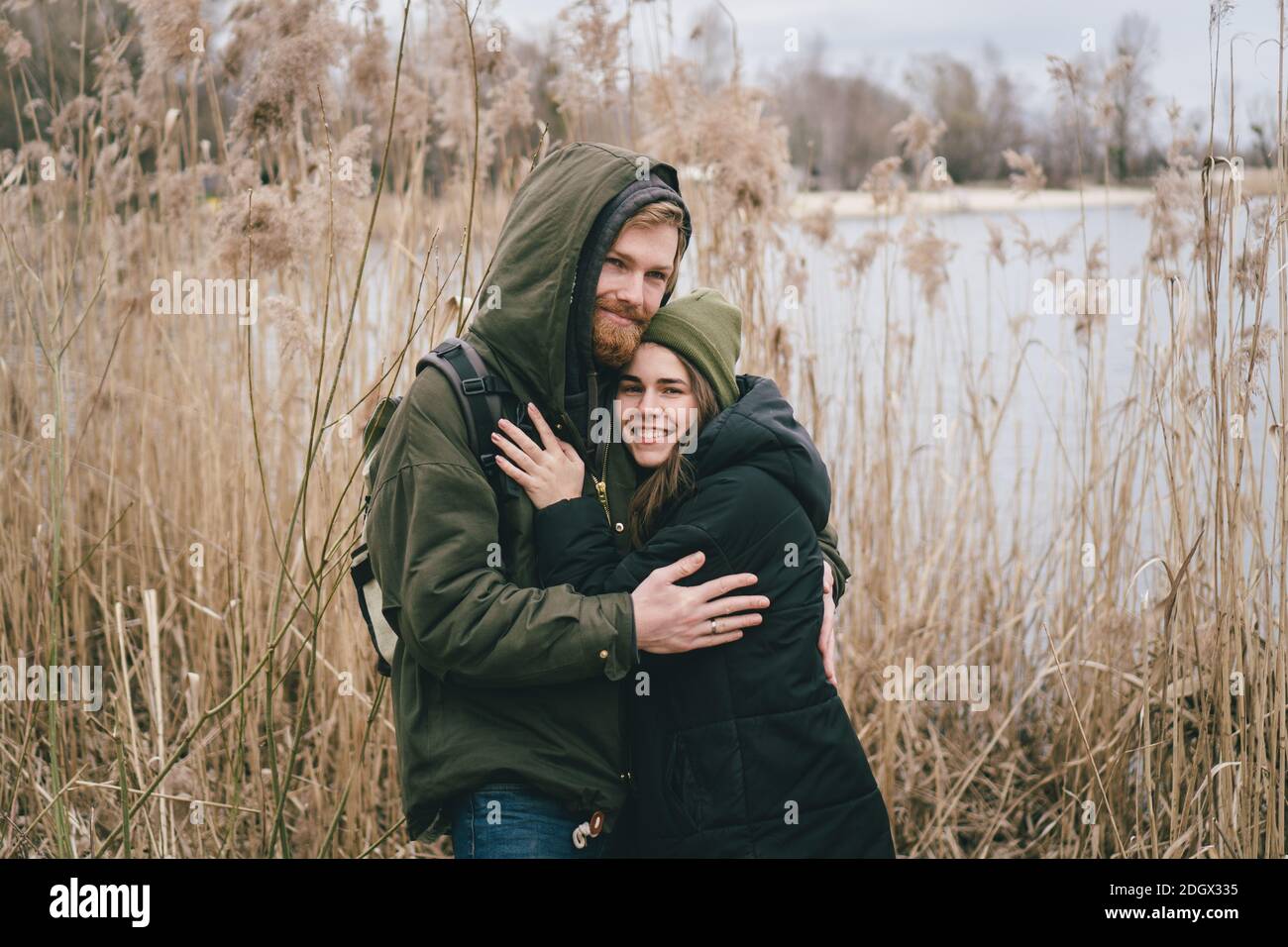 Ein junges kaukasisches Paar in der Liebe steht in einer Umarmung in der Nähe eines Sees und Schilf. Wochenenden und Spaziergänge in der Natur. Erholung im Freien Stockfoto