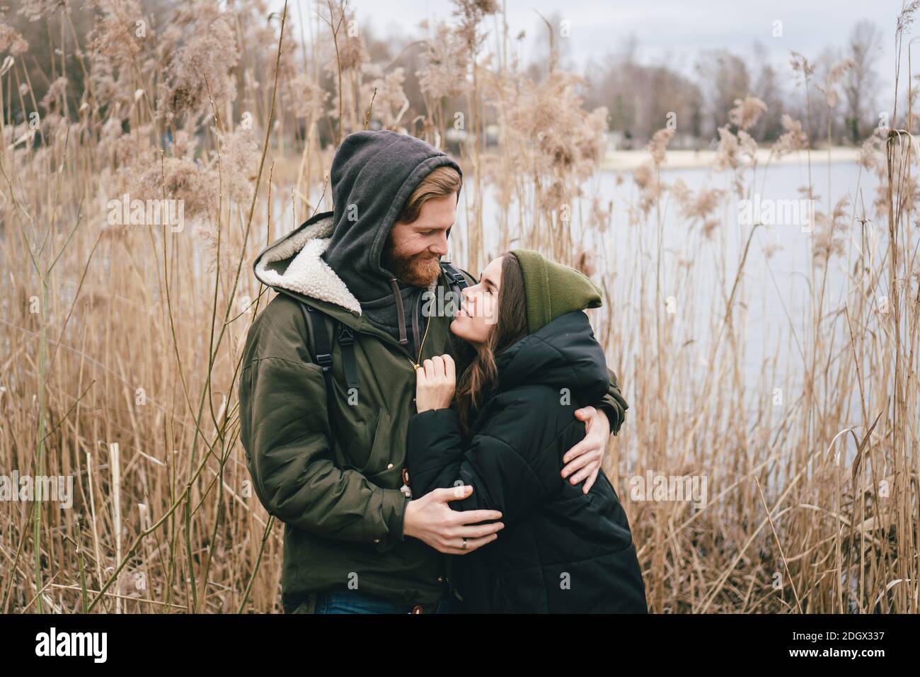 Ein junges kaukasisches Paar in der Liebe steht in einer Umarmung in der Nähe eines Sees und Schilf. Wochenenden und Spaziergänge in der Natur. Erholung im Freien Stockfoto