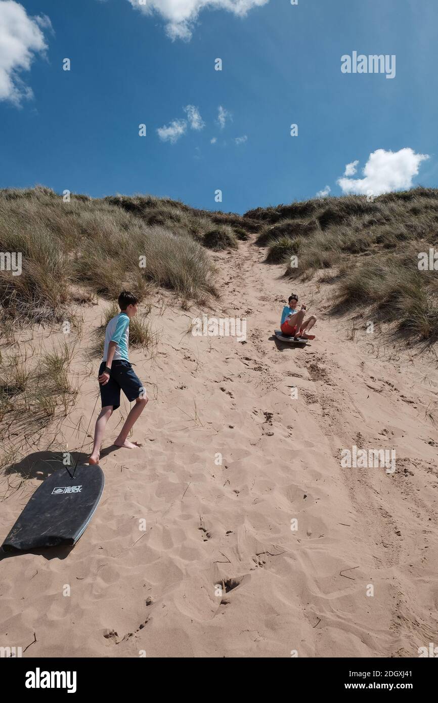 Zwei Brüder haben Spaß, während sie eine steile Sanddüne auf Bodyboards am Woolacombe Beach Devon hinuntergleiten. Stockfoto
