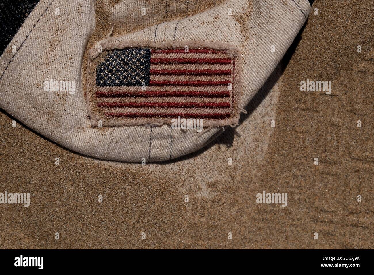 Amerikanische Flagge auf einer Baseballmütze, die im Sand vergraben ist, könnte als Konzeptbild für die Erforschung des Mondes verwendet werden. Stockfoto