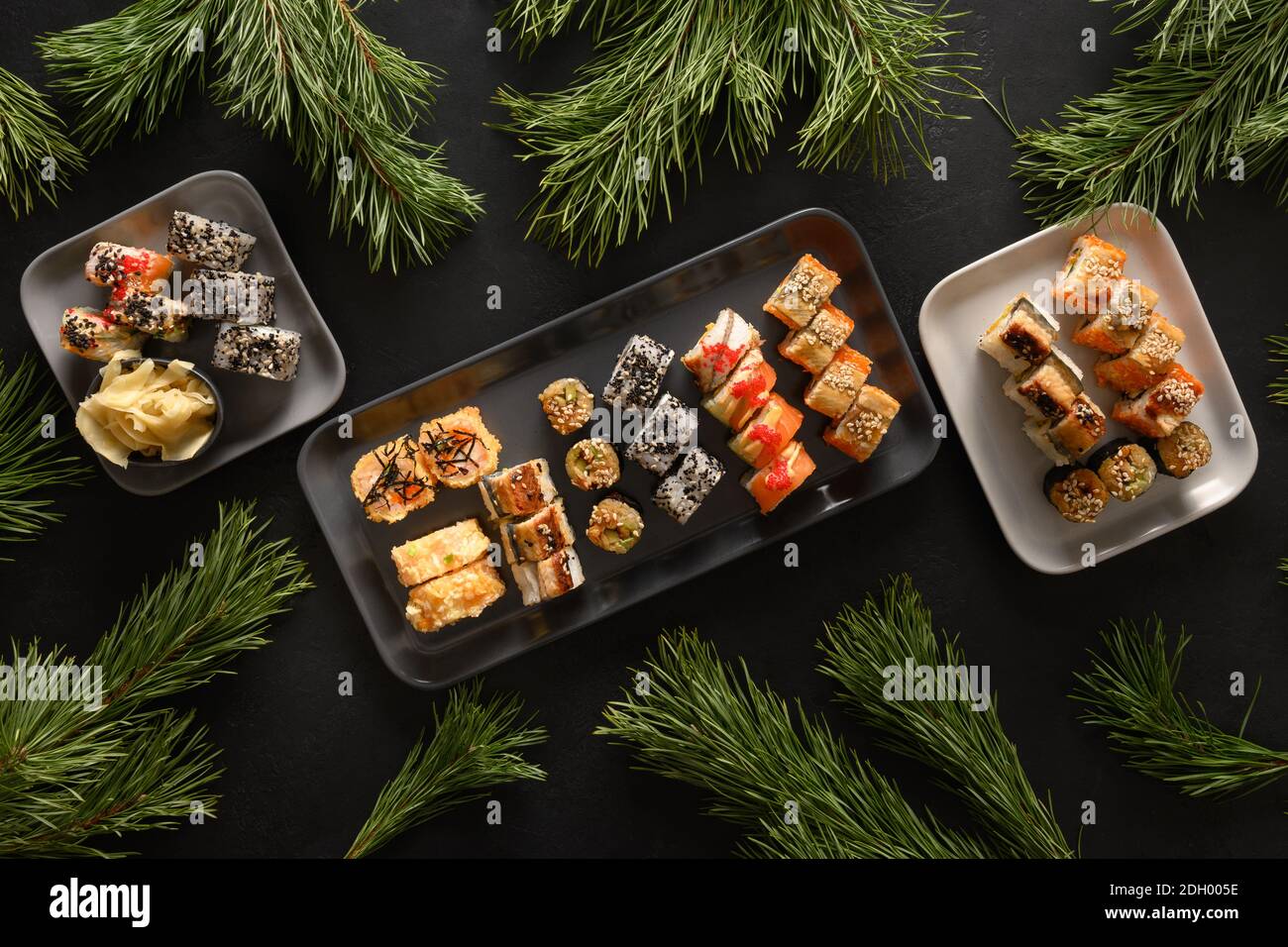 Weihnachtsessen mit Sushi-Set mit Weihnachtsdeko auf schwarzem Hintergrund. Blick von oben. Flache Lay-Optik. Weihnachtsfeier oder Neujahrsparty. Stockfoto