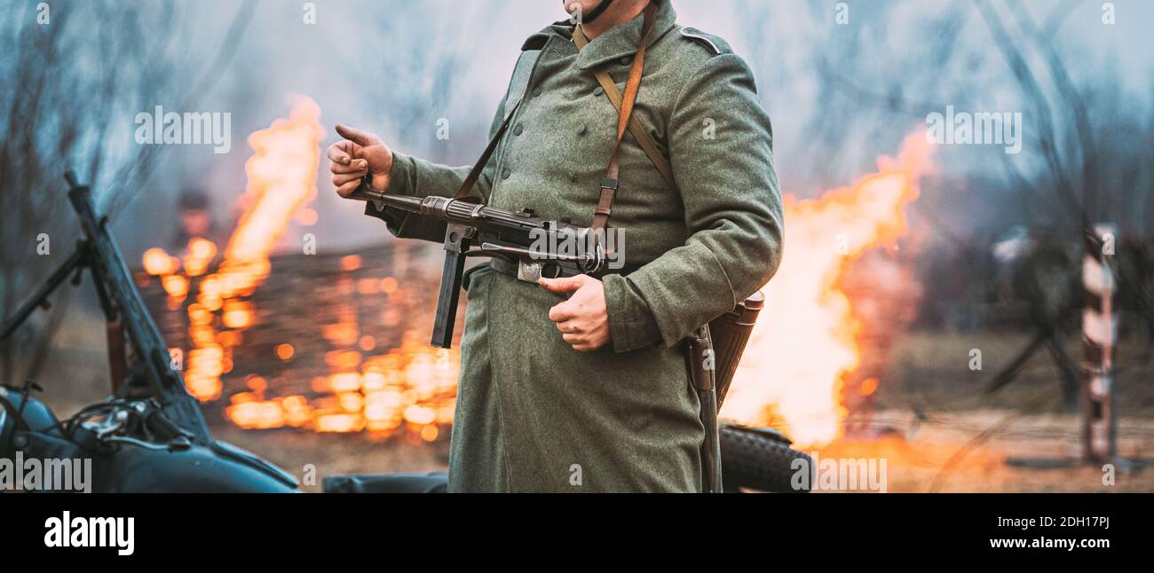 Re-enactor gekleidet als deutscher Wehrmacht Infanterie-Soldat im Zweiten Weltkrieg steht vor dem Hintergrund EINES brennenden Hauses. Deutscher Soldat des Zweiten Weltkriegs Stockfoto