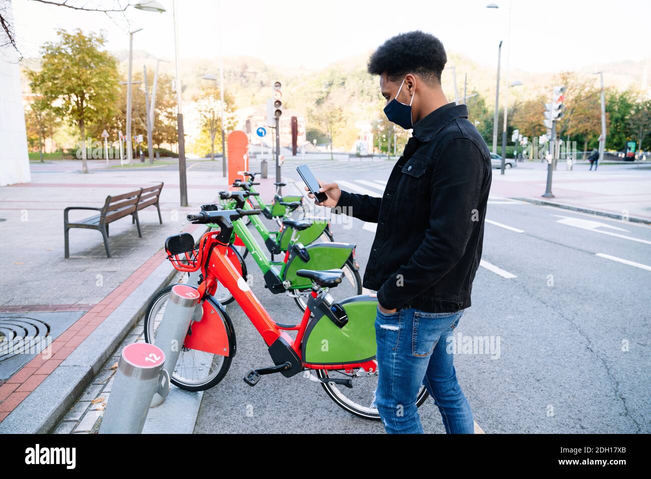 Junger marokkanischer Junge, der sein Handy benutzt, um abzuholen Ein ausgeliehenes Elektrofahrrad im Straßenfahrradpark und Trägt eine Gesichtsmaske zum 2020 covid19 coron Stockfoto