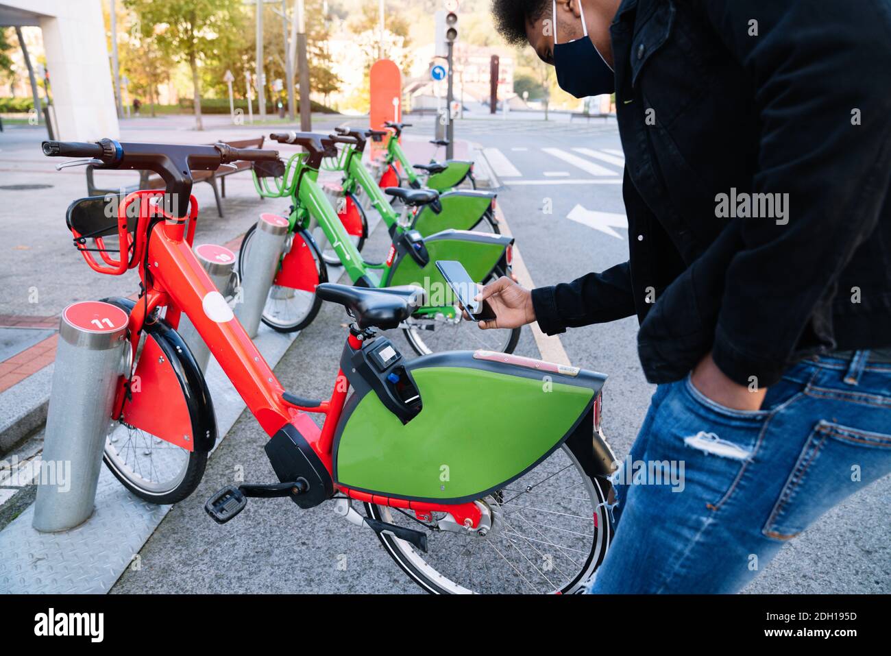 Junger marokkanischer Junge, der sein Handy benutzt, um abzuholen Ein ausgeliehenes Elektrofahrrad im Straßenfahrradpark und Trägt eine Gesichtsmaske zum 2020 covid19 coron Stockfoto