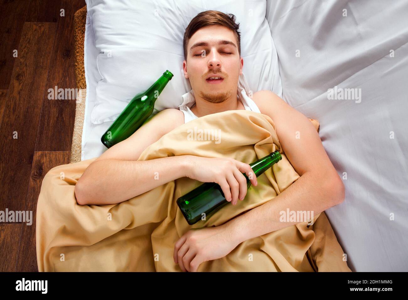 Junger Mann schläft mit einer Bierflasche im Bett Zu Hause Stockfoto