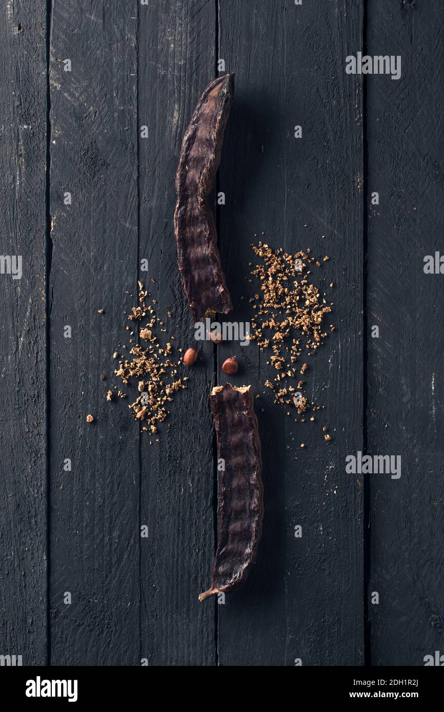 Geknackte Johannisbrotkapsel mit Samen auf schwarzem Holz Stockfoto