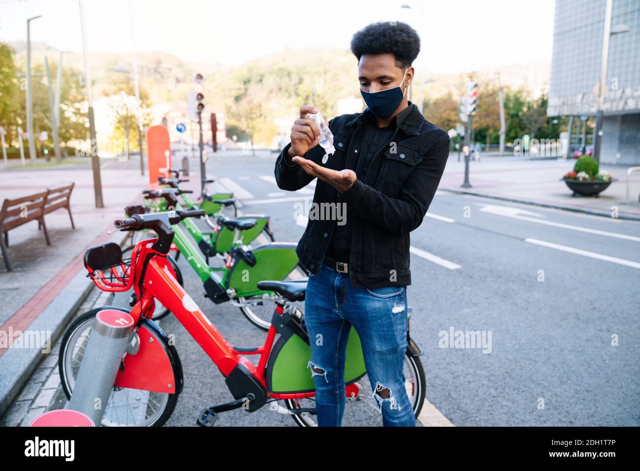 Ein junger Marokkaner gießt hydroalkoholisches Gel auf seine Hände, um ein ausgeliehenes Elektrofahrrad in der abzuholen Straße Fahrrad Parkplatz und trägt Stockfoto