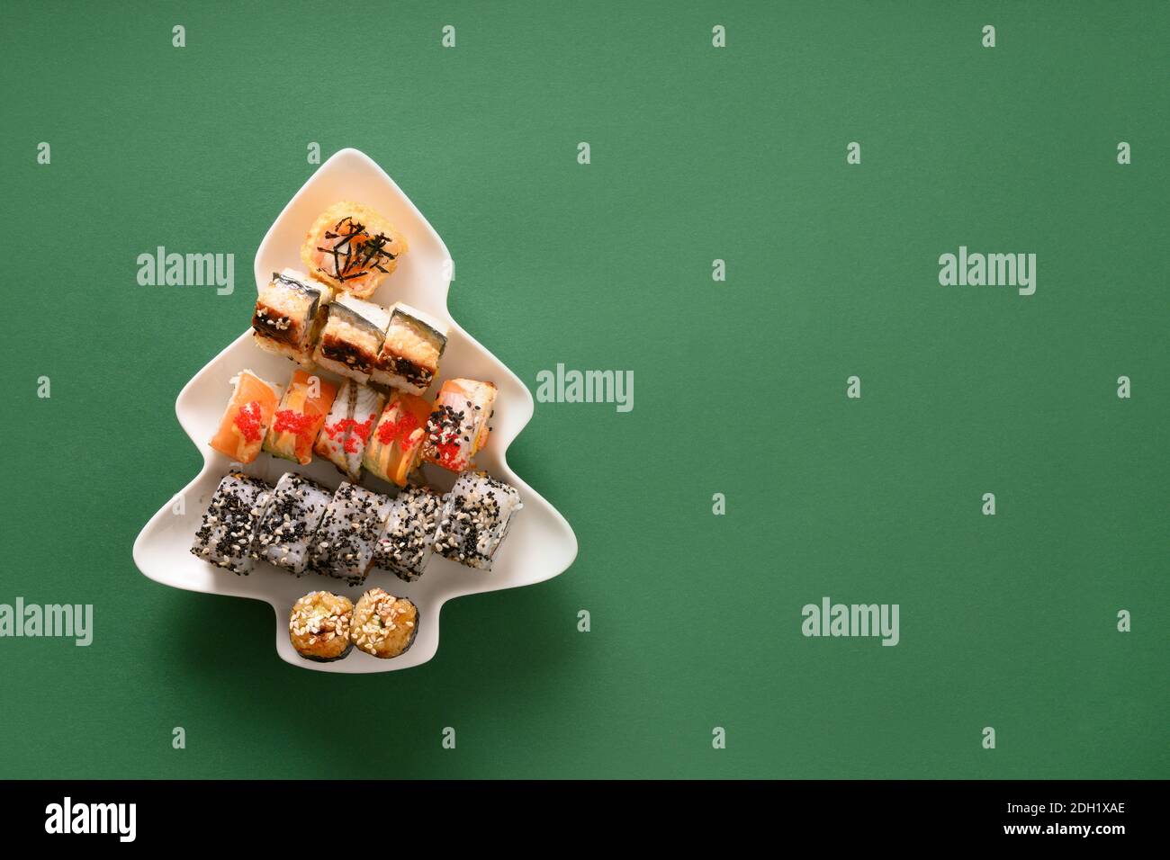 Sushi-Set in Teller als Weihnachtsbaum auf grünem Hintergrund dekoriert. Blick von oben. Leerzeichen für Text. Flatlay-Style. Stockfoto